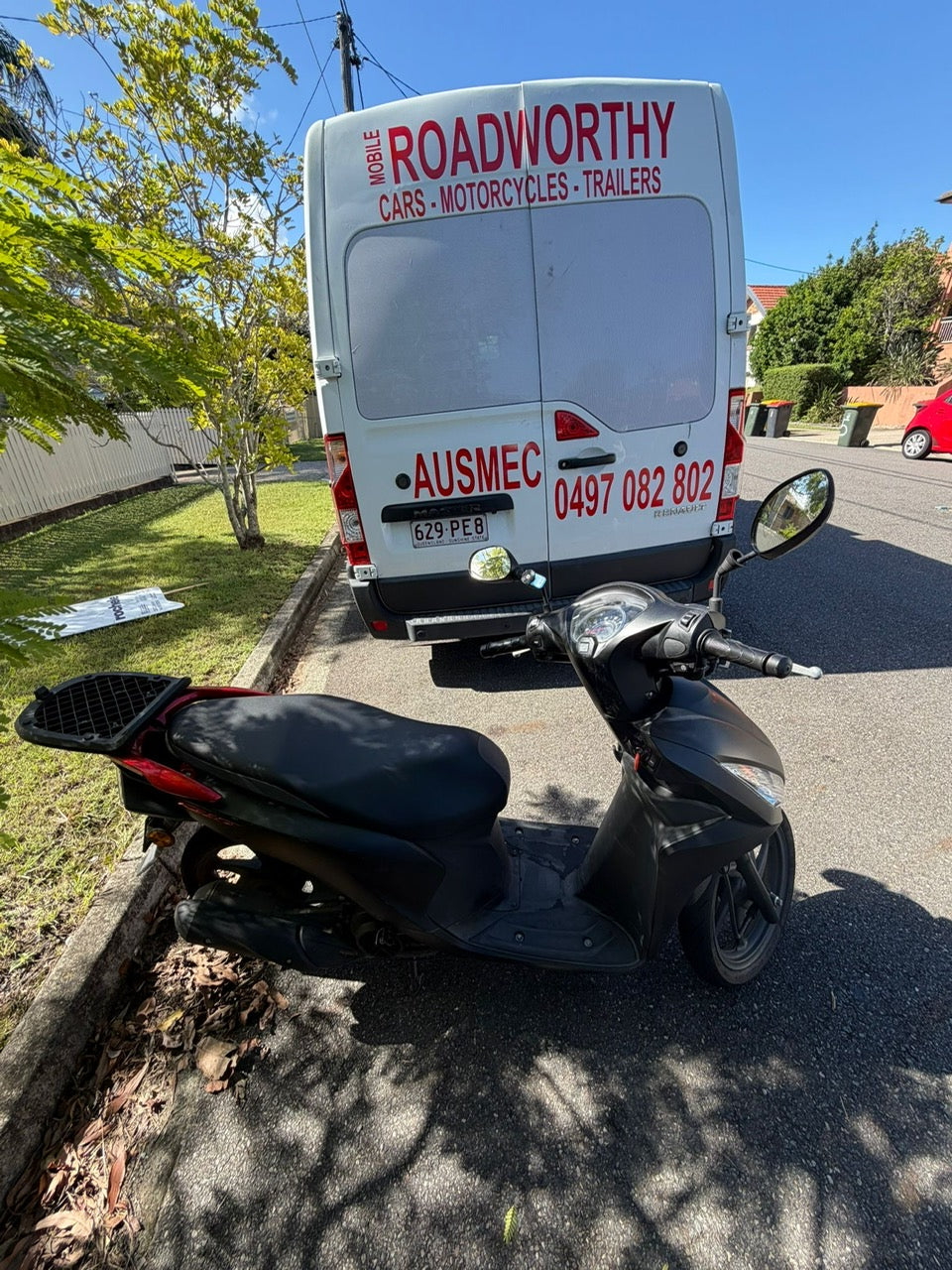 Black scooter parked on a street with a white van labeled 'Roadworthy' in the background in Strathpine