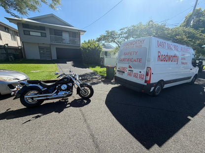White van with 'Roadworthy' branding parked on a street next to a motorcycle in Warner