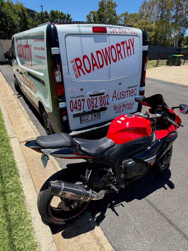Motorcycle parked next to a van with 'Roadworthy' branding on a street in Warner
