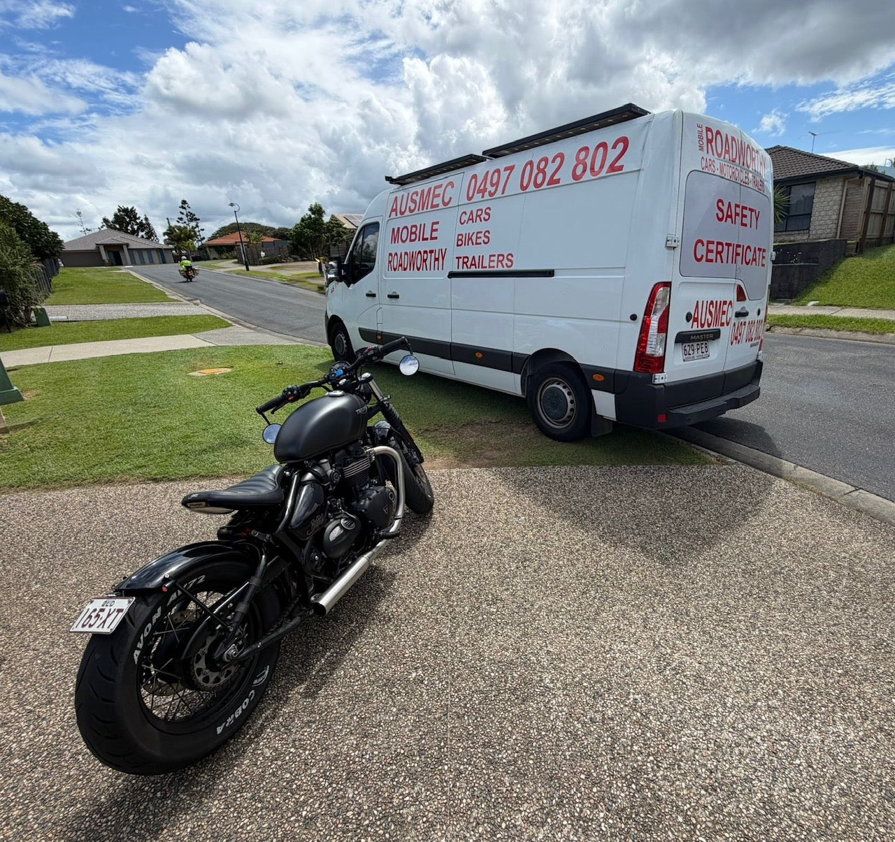 White Roadworthy Van with red text and a black motorcycle on a residential street in Wavell Heights