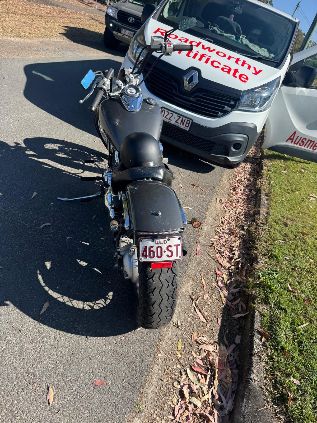 Motorcycle parked on the side of a road with a van in the background displaying a 'Roadworthy Certificate' in Zillmere.