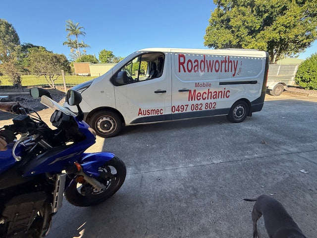 White van with 'Roadworthy' branding parked on a concrete surface next to a blue motorcycle.