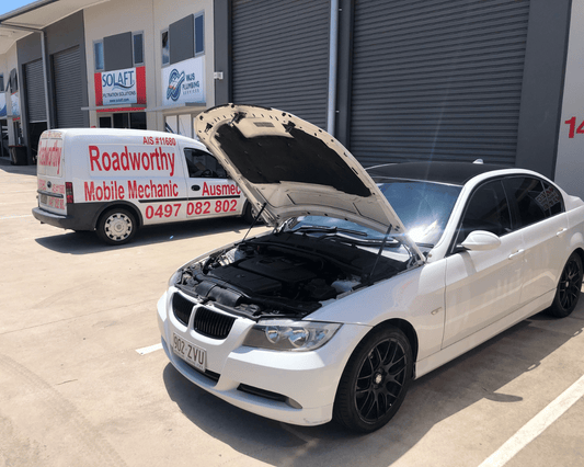 "Ausmec mobile mechanic performing a Narangba Mobile Roadworthy (Safety Certificate) inspection on a BMW car in a customer's car park." White car with open hood in front of a van labeled 'Roadworthy Mobile Mechanic'