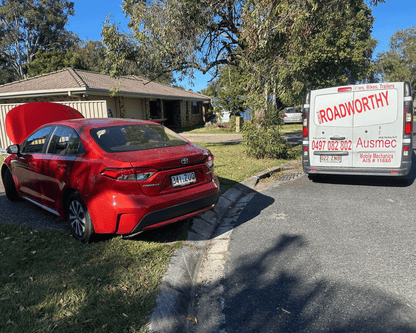 "Ensuring your vehicle's safety with a comprehensive Taigum Mobile Roadworthy (Safety Certificate)." Red car with open hood on a driveway next to a van with 'Roadworthy' signage.
