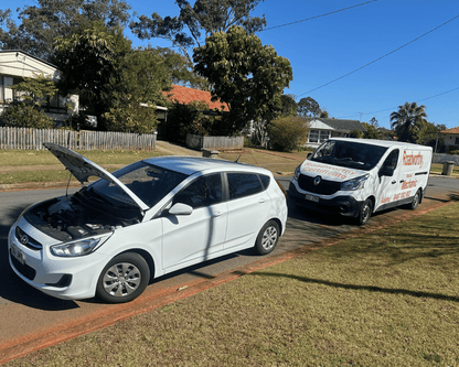 "Convenient Burpengary Mobile Roadworthy (Safety Certificate) for a car being conducted by an Ausmec mechanic at a customer's home." White car with open hood on a driveway next to a van with a visible brand logo.