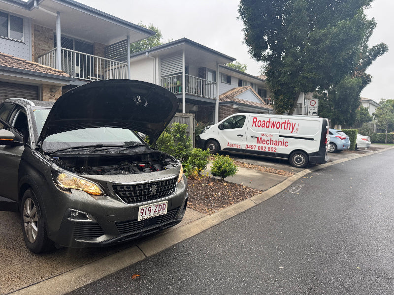 A complete pre purchase car inspection Near Albion, including a full scan and thorough check of the vehicle in the seller's driveway. Car with open hood on a residential street, Radworthy van parked nearby